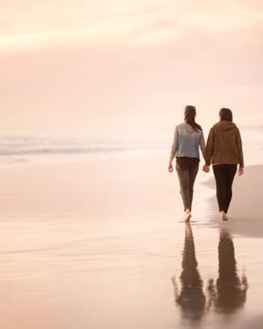 Couple holding hands as they walk along a quiet beach in soft morning light