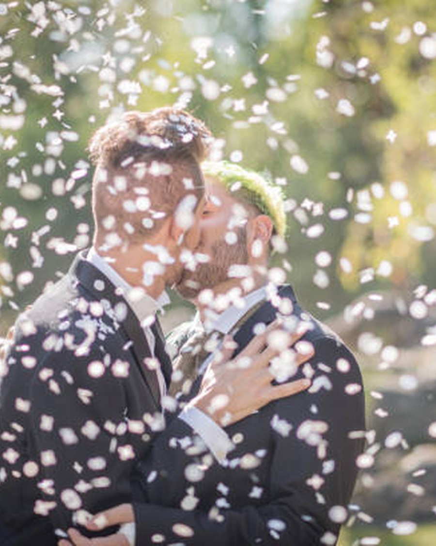 Two grooms kissing beneath a shower of petals after their wedding